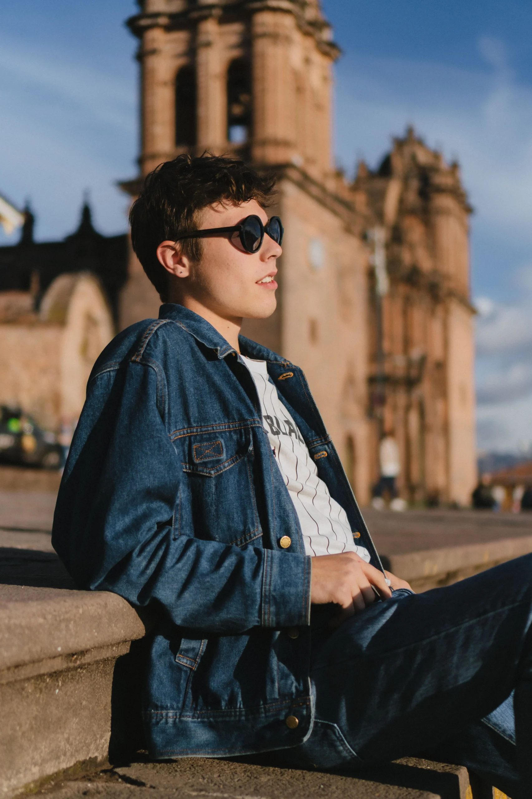 Man posing in front of the church in Cusco wearing sunglasses and denim.