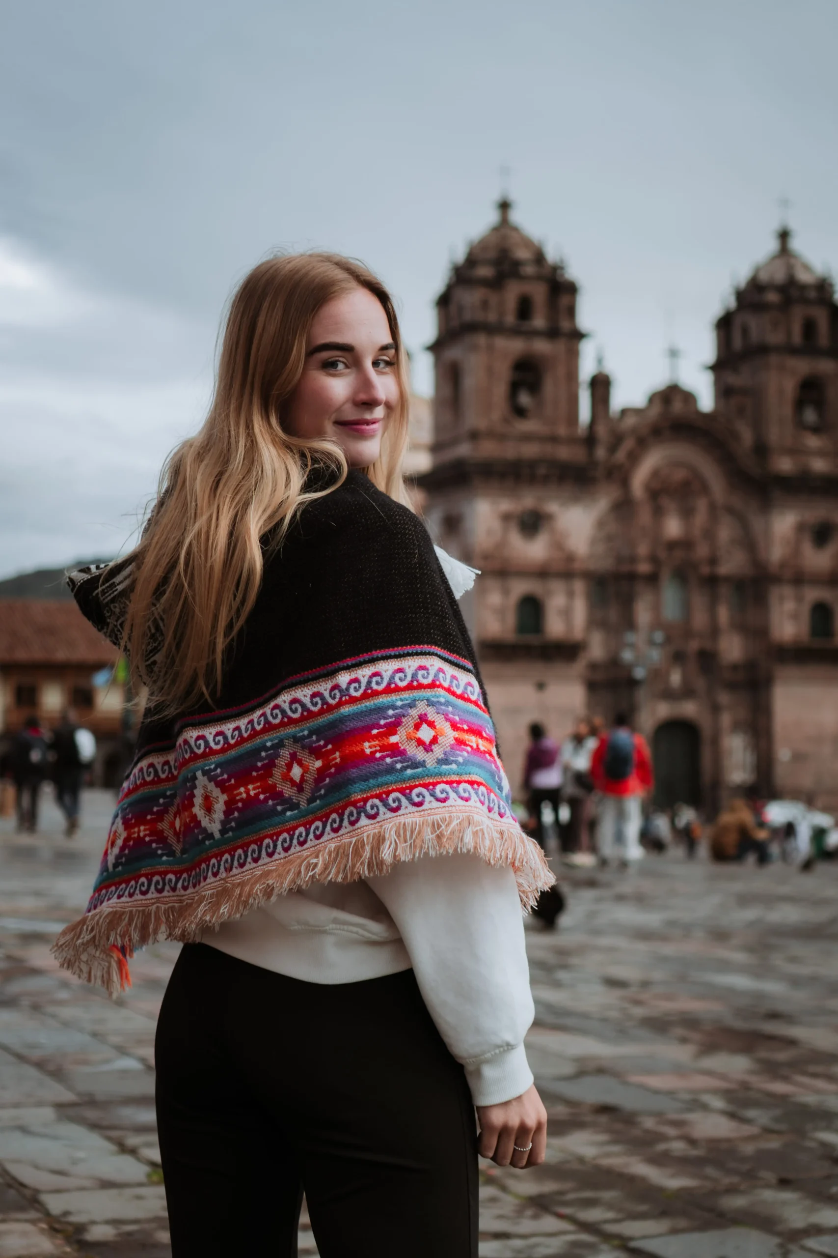 Woman in traditional poncho posing in front of Cusco Cathedral.